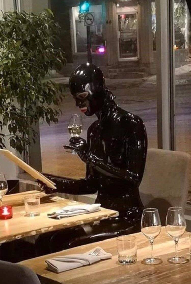 The meme features a person dressed in a black rubber bodysuit, sitting at a restaurant table, and holding a wine glass. The image is captioned "I'm not arguing, I'm just explaining why I'm right". The meme is humorous because it's a relatable situation where someone is trying to be assertive or persuasive, but is actually just being stubborn and argumentative.